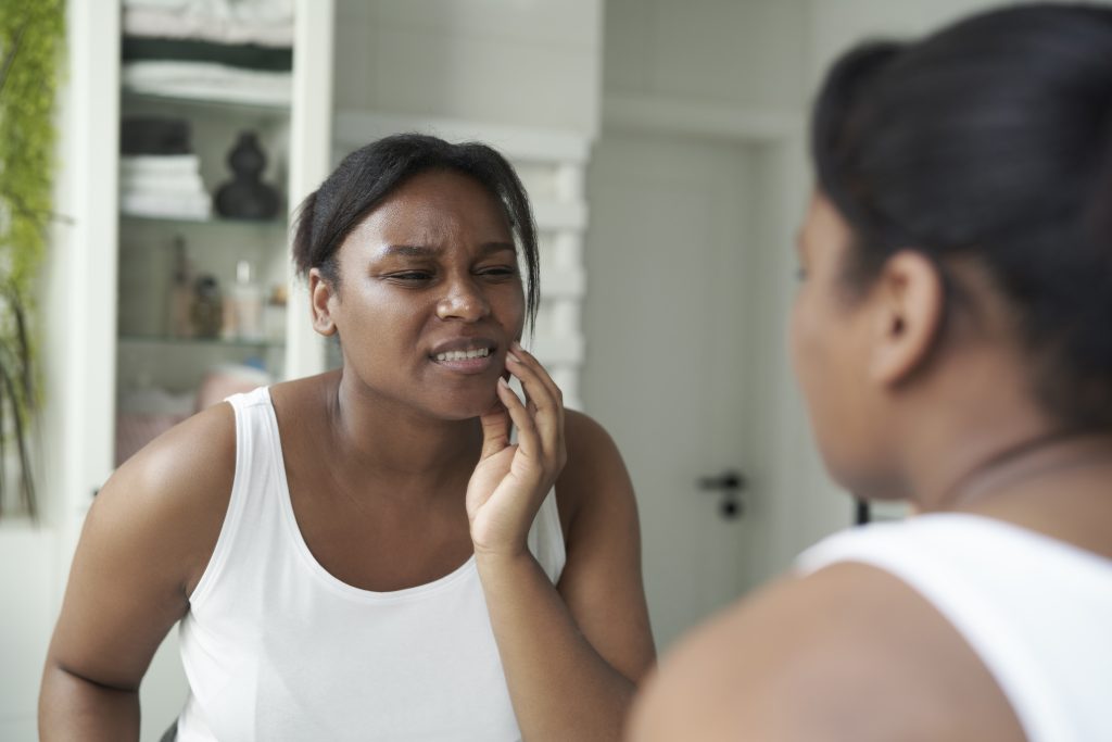 African-American woman in the bathroom having a strong toothache or bruxism